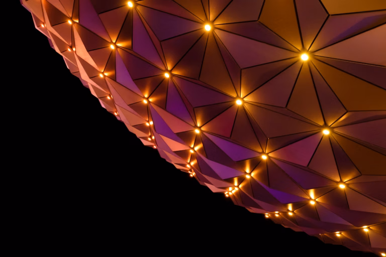 Underside of a faceted geodesic dome glowing with warm gold and purple lights against night sky